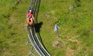 A man rides an alpine coaster on a green slope overlooking the village of Oberammergau, Germany.