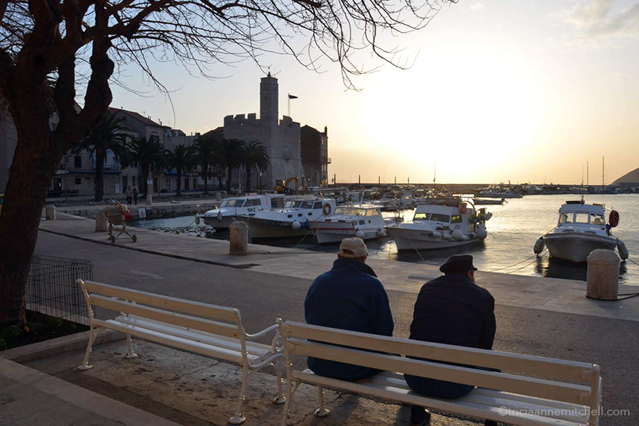 Two men wearing hats sit on white benches watching a sunset in Craotia.